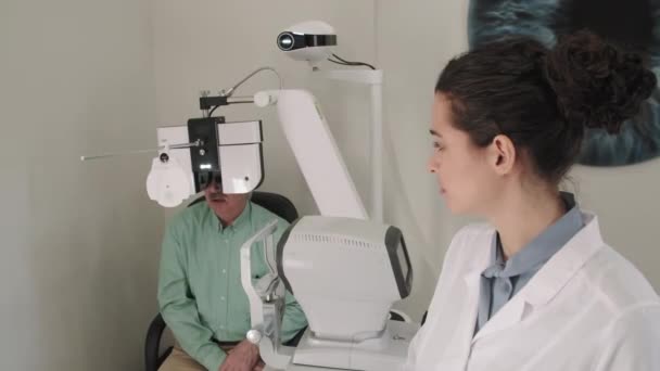 Средний План Женщины Офтальмолога Наблюдающей Старшим Мужчиной Делающим Осмотр Глаз — стоковое видео