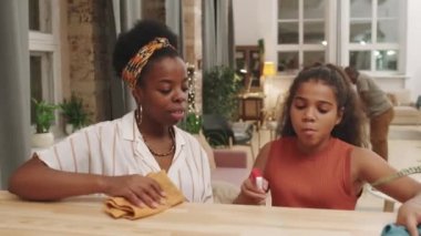 Dört çocuklu mutlu Afro-Amerikan aile evlerinde ev işleri yaparken belden yukarısına çekilen fotoğraf. Anne ve kızı toz alırken sohbet ediyorlar.