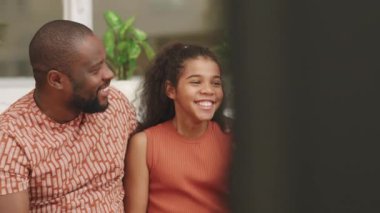 Yavaş çekim, orta ölçekli mutlu Afro-Amerikan aile gülüşü TV programını tartışırken birlikte kanepede otururken.