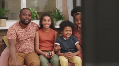Oturma odasındaki rahat koltukta oturup sohbet eden dört kişilik neşeli Afro-Amerikan aile fotoğrafı. Birlikte televizyon seyrederken.