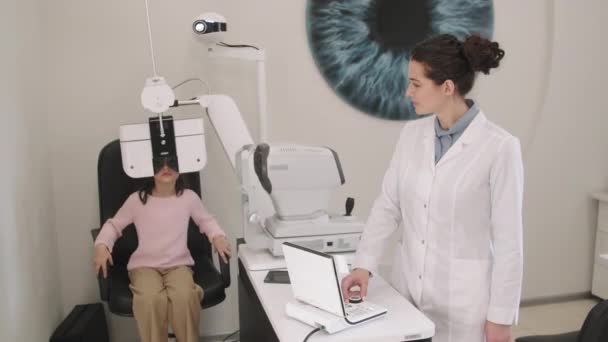 中出しの女の子と女性眼科医あります定期的な目の検査でクリニックで現代的な光学機器 — ストック動画