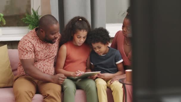 10岁女孩坐在沙发上玩数字平板电脑游戏的快乐的四口非洲裔家庭中的Pan镜头 — 图库视频影像