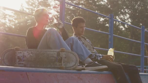 Handheld Slow Tiro Adolescentes Sentados Topo Rampa Parque Skate Beber — Vídeo de Stock