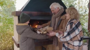 Orta yaşlı, beyaz bir adam ve karısının şöminenin önünde kalın giysiler giyip ellerinde torunlarının odunlarıyla sepet taşırken çekilmiş bir fotoğrafı.