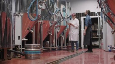 Kadın sağlık müfettişi bira fabrikasını incelerken fabrika boyunca bira fabrikasında işçi eşliğinde detayları anlatırken tam açılı bir fotoğraf.