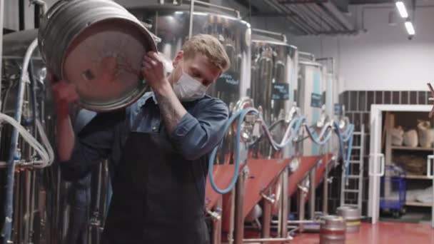 スローモーション中出しの強い残忍な男のショットで保護マスク作業で醸造所重いビール樽を運ぶ — ストック動画