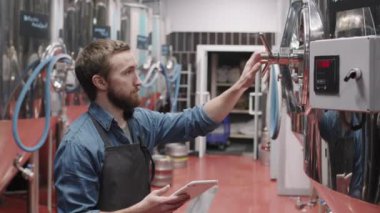 Dijital tabletli erkek bira fabrikası işçisinin fabrikada bira üreten depolama tankına parametreler koymasıyla yan görüş ortamı yakın çekim