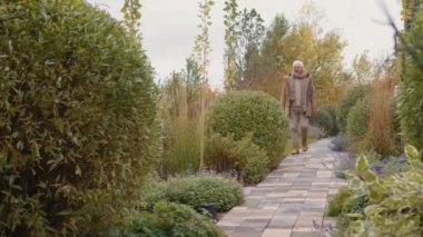 Kafkas 'lı üst düzey bir adamın kalın giysiler ve gözlük takıp güzel bir bahçede yürüdüğü ve bitkilerin tadını çıkardığı geniş bir çekim.