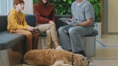 Sahipleri profesyonel erkek veteriner ile konuşurken Golden Retriever köpeğinin veteriner kliniğinin zemininde dinlenmesi.