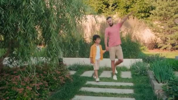 一群英俊的大胡子男人和他可爱的儿子穿着休闲装 沿着美丽的后院散步 欣赏着植物和花朵 — 图库视频影像