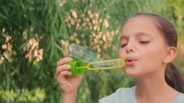 Yavaş çekimde, yaz aylarında dışarıda sabun köpüğü üfleyen 10 yaşında tatlı bir kızın yakın çekimi.