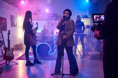 Şarkıcı mikrofonda şarkı söylüyor ve gece kulübünde müzik grubuyla şarkı söylüyor.