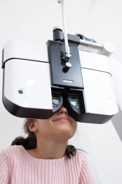 İlkokul çocuğu, çağdaş kliniklerde görme yeteneği kontrol edilirken göz hekimliği aletlerinin önünde oturuyor.