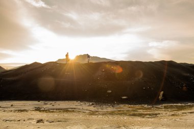 İki çağdaş araştırmacının küçük siluetleri gün batımında gri bulutlu gökyüzüne karşı tepenin üstünde duruyor.