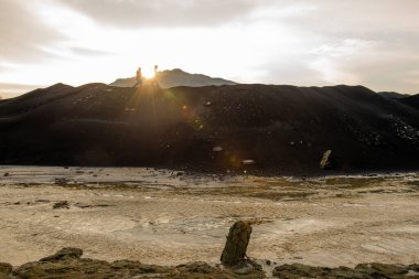 İki ekolojist ya da araştırmacının küçük siluetleri gün batımında parlak güneş ışığıyla gri bulutlu gökyüzüne karşı tepe boyunca ilerliyorlar.