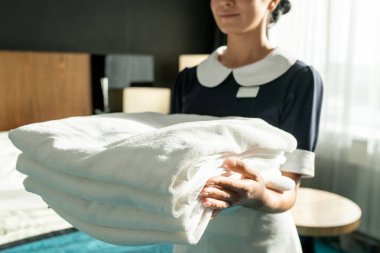Bir el dolusu temiz çarşaf ya da havlu taşıyan üniformalı güzel oda hizmetçisi otel odasında ayakta dikilirken
