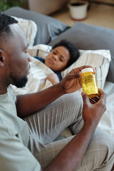Fiatal Óvatos Apa Kezében Üveg Pirulák Miközben Ágyon Mellett Beteg — Stock Fotó