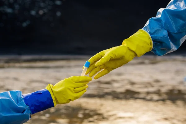 生态学家戴着手套的手 穿着防护服 从同事身上取出装有有毒水样本的瓶子 以防止污染河流 — 图库照片