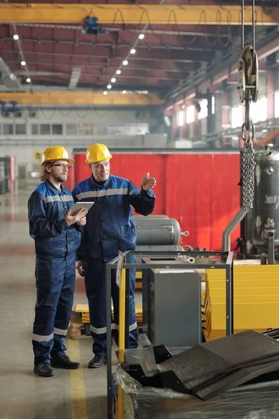 两名工程师站在大型车间或工厂 讨论新的工业设备或机器 其中一人指着它 — 图库照片