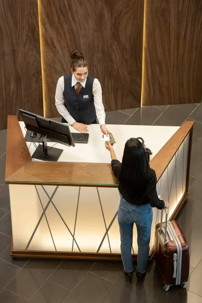 現代的なホテルのロビーで受付カウンターの上に女性旅行者に職場やパスポートを渡すことで統一された立場の若い受付係 — ストック写真