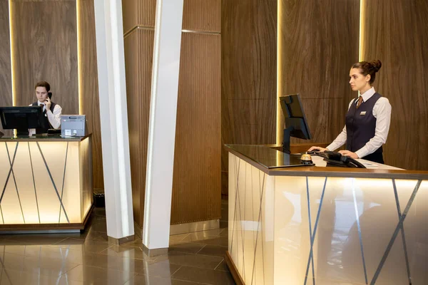 Jonge Elegante Vrouwelijke Receptioniste Uniform Staat Bij Balie Kijkt Naar — Stockfoto