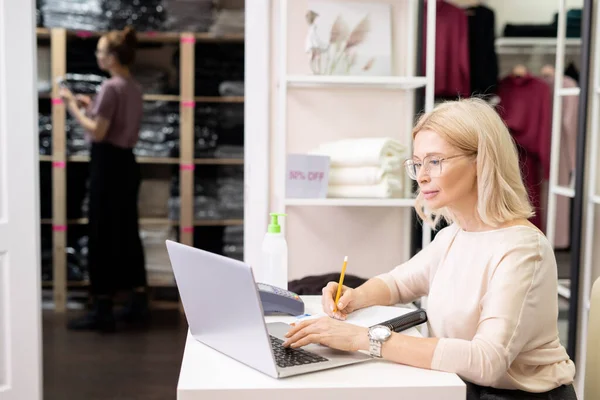成熟した実業家は テーブルに座って 衣料品店でラップトップで作業 — ストック写真