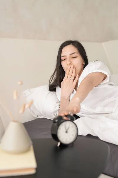 Jovem Morena Sonolenta Com Pijama Branco Bocejando Pressionando Botão Despertador — Fotografia de Stock