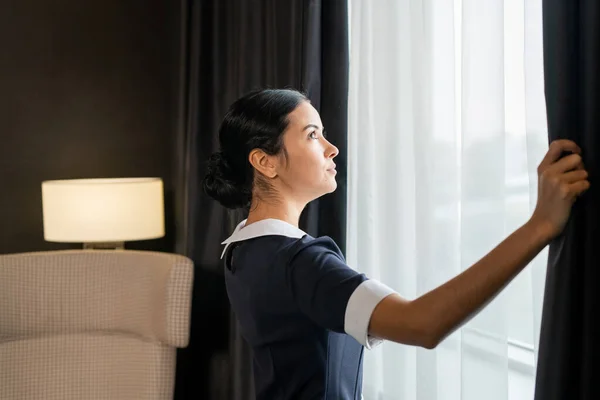 Vista Laterale Della Giovane Cameriera Uniforme Aprendo Tende Scure Una — Foto Stock