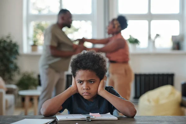 愤怒的非洲裔小男孩一边用手捂住耳朵 一边做功课 反对父母争吵 — 图库照片