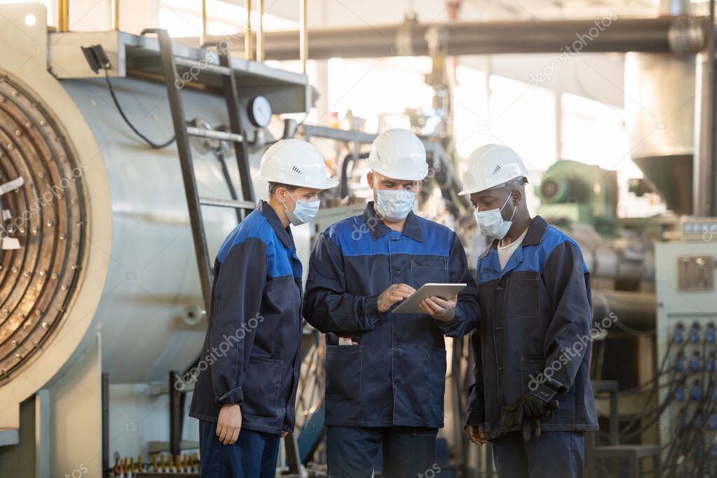 Group of young contemporary workers of modern plant looking through online sketches of details for industrial machines in workshop