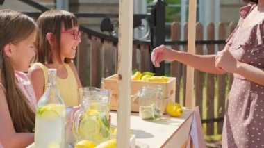 10 yaşındaki iki kızdan taze yapılmış limonata alan yaz polka elbiseli çekici bir kadının orta boy pozunu çek.