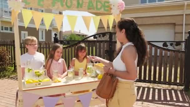 夏天阳光明媚的日子里 站在室外 一个快乐的女人正在给孩子们买新鲜的自制柠檬汁 — 图库视频影像