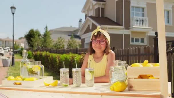 ウエストアップポートレートの陽気10歳の女の子で眼鏡販売新鮮な自家製レモネード屋外で暑い夏の日にカメラに笑顔 — ストック動画