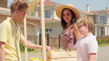 Yazın açık büfeden taze limonata alan bir çocuğun orta boy fotoğrafı. Dost canlısı anne ve oğul güneşli bir günde ferahlatıcı içecekler satıyorlar.