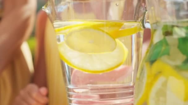 夏の暑い日に屋外で作る新鮮なレモネードのガラスのデカンタにレモンスライスを追加します — ストック動画