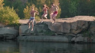 Bir grup mayo giymiş genç arkadaşın yaz aylarında uçurumdan göle atladığı PAN yavaş çekim.