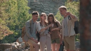 Sırt çantalı bir grup gencin ormanda yürüyüş parkurunda durup cep telefonlarındaki haritaya baktıkları görüntüleri. Yol tarifi tartışıyorlar ve gülüyorlar.