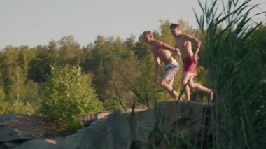 Mayo giymiş kaygısız gençleri yavaş yavaş takip ediyor yaz günü küçük bir uçurumdan göle atlayıp koşuyorlar.