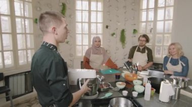 Modern aşçılık okulunda yemek kursu sırasında dört kişilik bir grubun önünde duran ve mikser makinesini düzgün kullanmayı öğreten genç ve kendine güvenen şefin yavaş çekimleri.