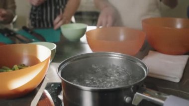 Yemek pişirme kursu, şef ve küçük bir grup insan arka planda durup yemek pişirmeyi öğretirken demlikte kaynayan suya yakın durun.