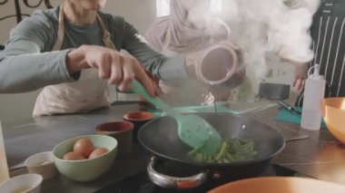 Aşçılık kursunda yemek pişirme pratiği yapan ve kızarmış yeşil fasulyeye soya sosu ekleyen tanınmayan bir kadının yavaş çekimleri.