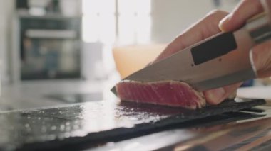 Mutfakta şef bıçağıyla kurutulmuş ton balıklı bifteği dikkatle dilimleyen tanınmayan erkek ellerini kapatın.