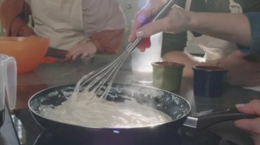 Aşçılık kursunda yavaş çekimde, tanınmayan bir kadının krema sosu yaparken görüntüsü.