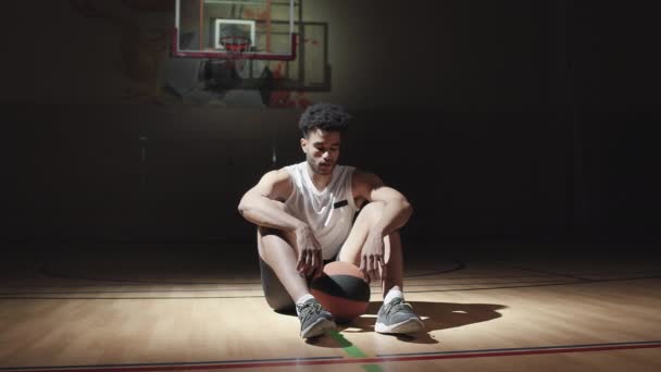 Фотография Молодого Чернокожего Мужчины Спортивной Одежде Сидящего Полу Баскетбольной Площадке — стоковое видео