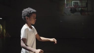 Siyah sahada antrenman yaparken yakışıklı Afro-Amerikan bir çocuğun basketbol topunu yakalayıp pas attığı yavaş çekim.