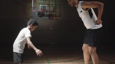 Profesyonel erkek basketbolcunun, çocuklara kapalı sahada top sürmeyi öğrettiği orta boy bir fotoğraf.