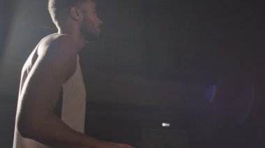 Siyah erkek basketbolcunun kapalı alanda topa vuruşunun yavaş yan görüntüsü.