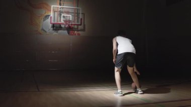 Spor giyimli erkek basketbolcunun yavaş çekimde top sürerken ve potaya atarken.