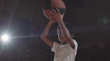 El kamerasıyla, elinde basketbol topu tutan Afro-Amerikalı bir çocuğun kapalı sahadaki potaya yaptığı atış.