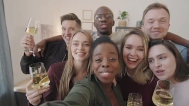 Mutlu erkek ve kadınların ellerinde şampanya ya da beyaz şarap kadehleriyle ev partisinde selfie çektikleri poz.